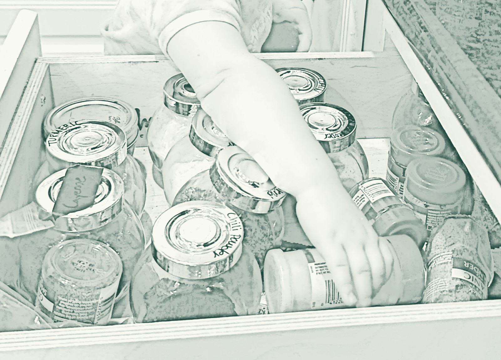 A small hand reaching into an open drawer of labeled spice jars