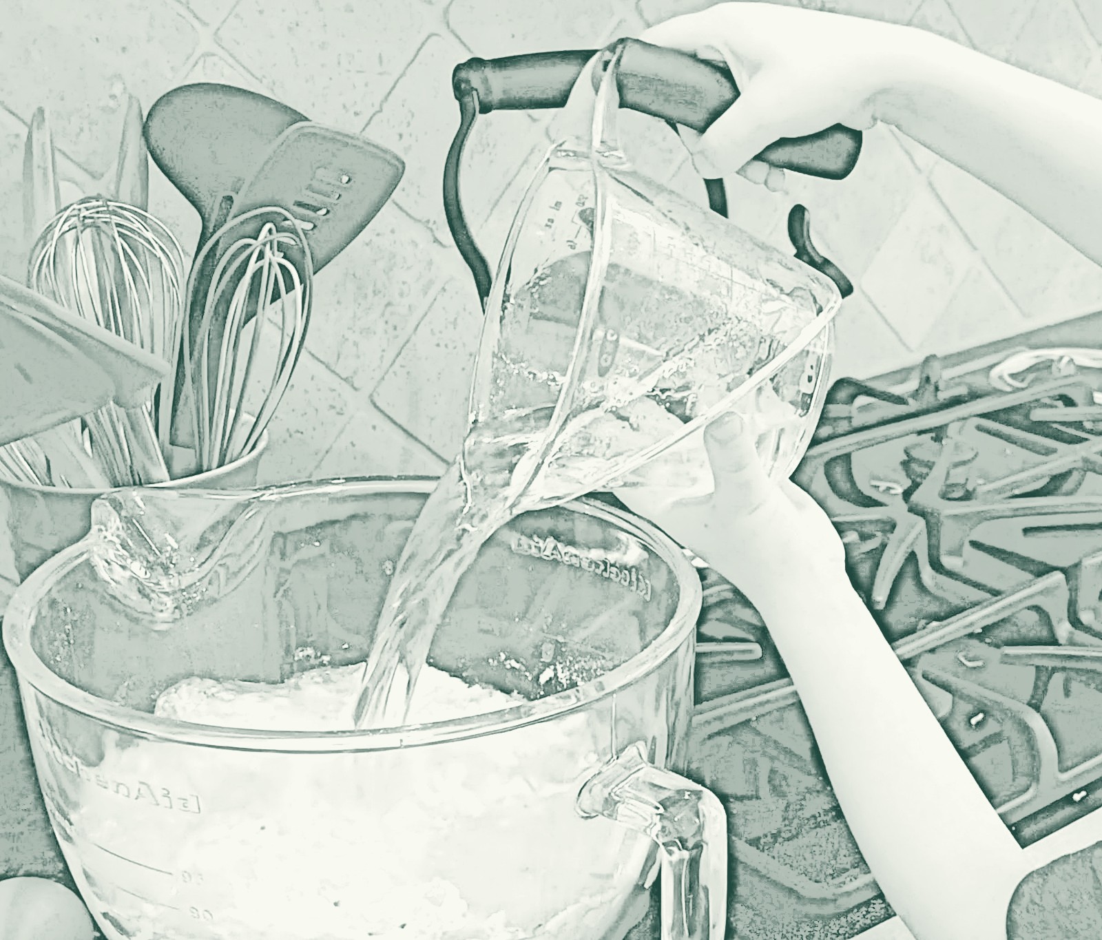A child's hands tipping a glass measuring cup of water into the bowl of a stand mixer